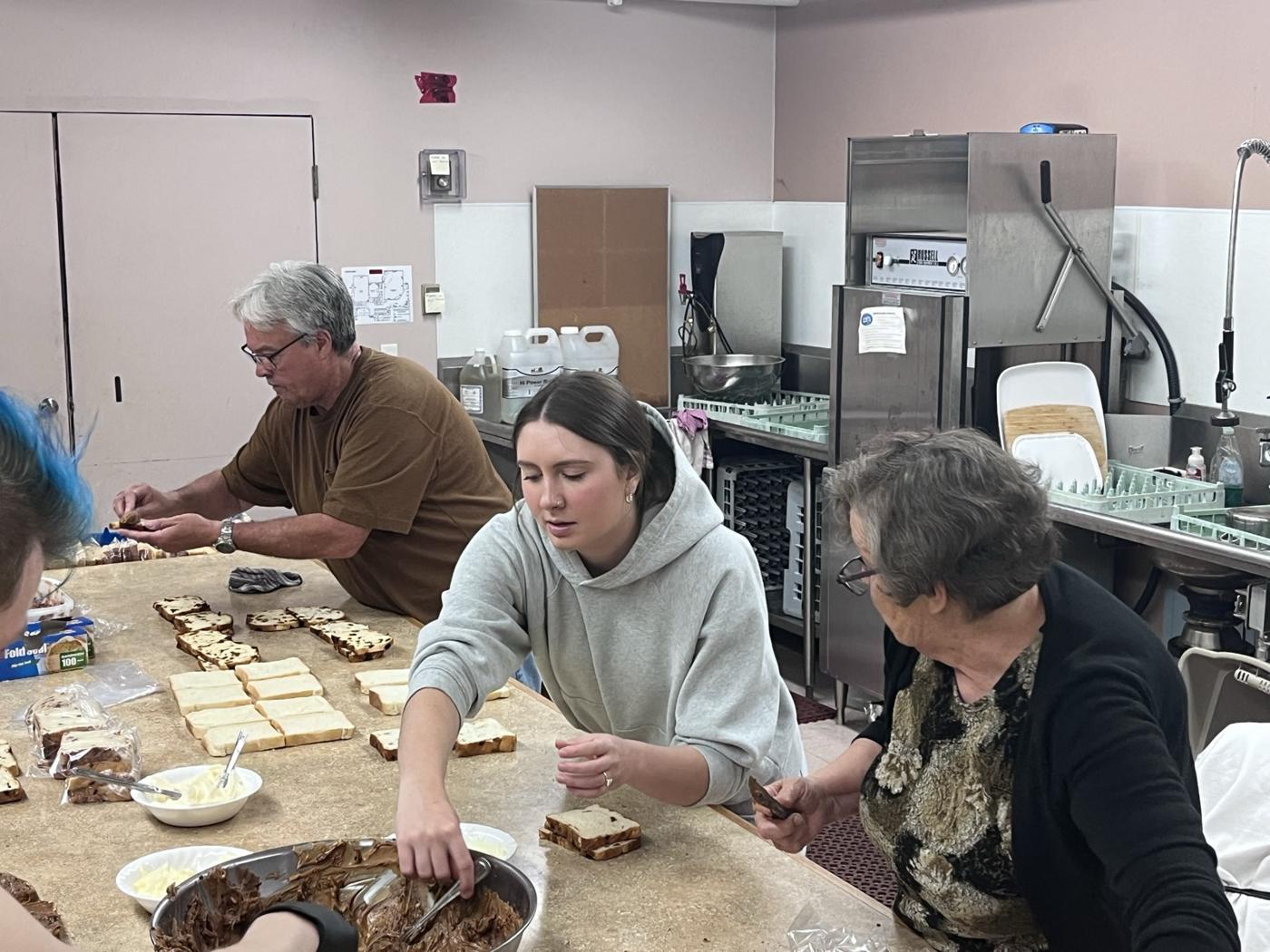 Volunteers of all ages making sandwiches around a kitchen counter
